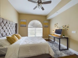 A charming apartment rental with cheerful yellow accents and a refreshing ceiling fan in the bedroom.