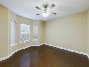 An empty room with brown floors and a ceiling fan.